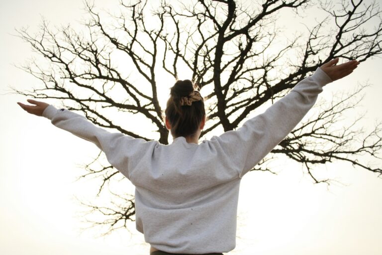 Woman arms stretched in front of tree.